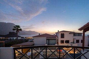 Une propriété située sur la côte, dotée d’un balcon, avec une montagne en arrière-plan et un coucher de soleil.