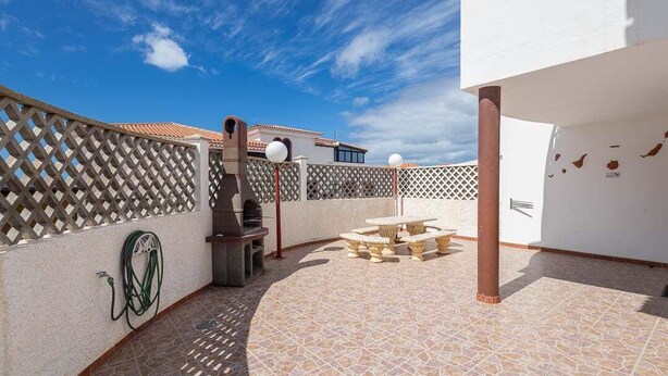 A patio with a grill, outdoor seating, and a hose.