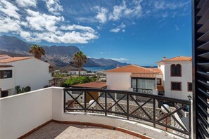 A balcony with a view of a coastal town, mountains, and a clear sky.
