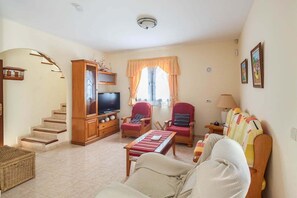 A living room with a TV, two red chairs, a sofa, a lamp, and a window with curtains.