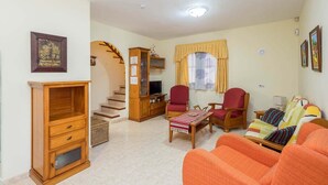 A living room with a sofa, chairs, a wooden cabinet, a television, and a staircase.