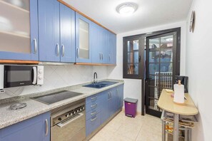 Una cocina con gabinetes azules, un microondas, un lavamanos y una pequeña mesa con un cubo de basura.