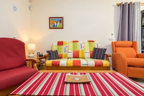 Una sala de estar con un sofá, sillones, un tapete a rayas, un cuadro en la pared y una ventana con cortinas.