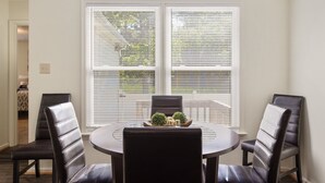 A dining area with a round table, four chairs, and a window with blinds.