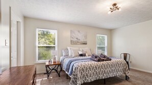 A bedroom with a bed, a desk, a chair, and a window.