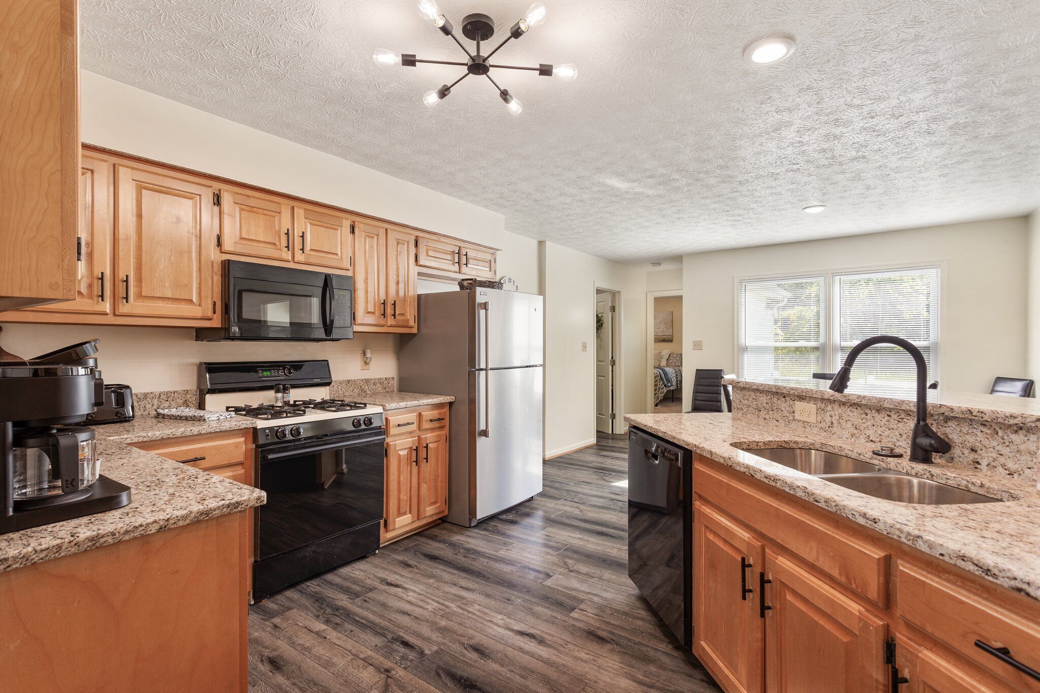 A kitchen with wooden cabinets, a stainless steel refrigerator, a microwave, a stove, and a sink.