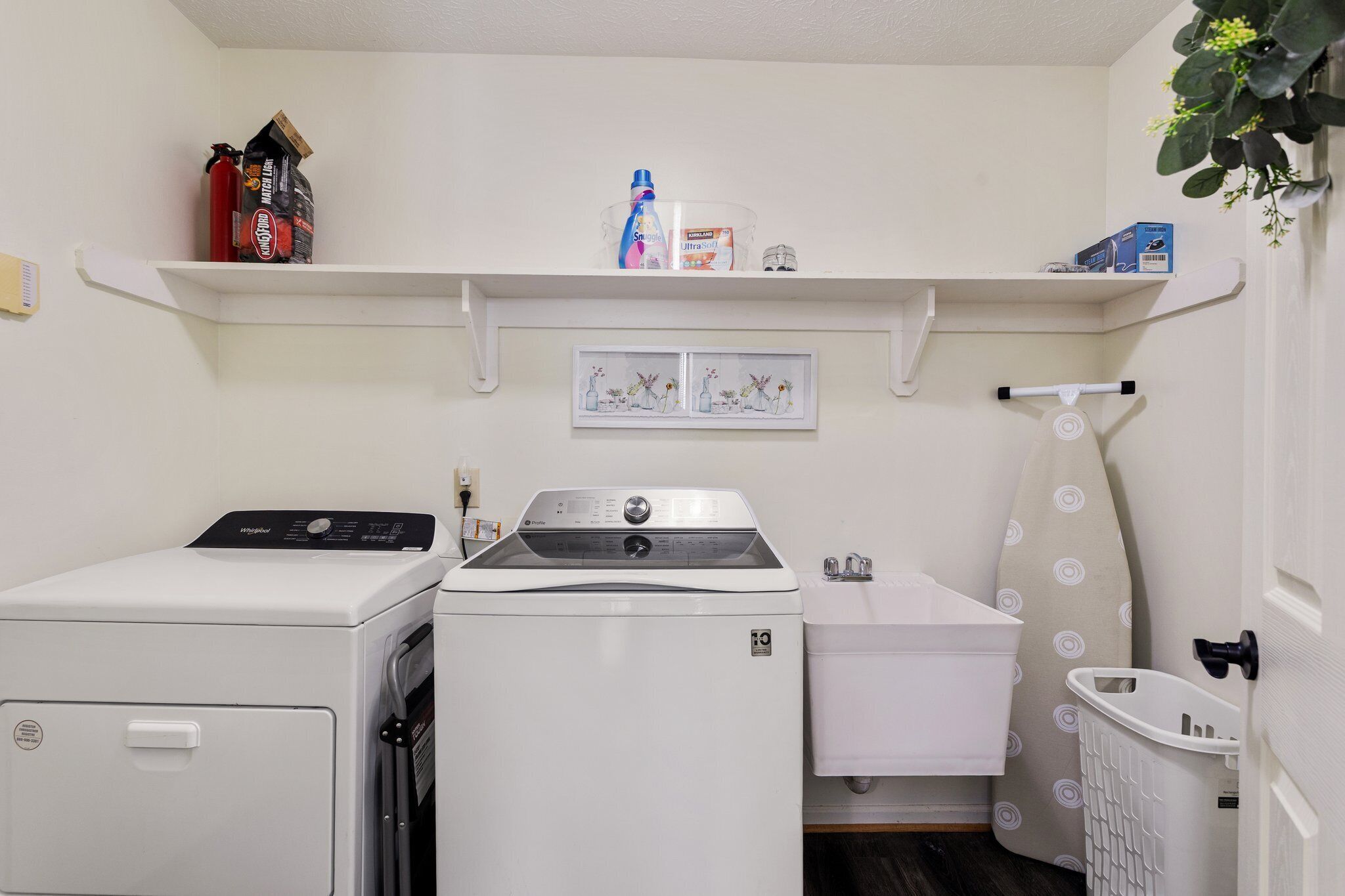 Un espace buanderie équipé d’un lave-linge, d’un sèche-linge et d’étagères où sont rangés les produits de nettoyage.