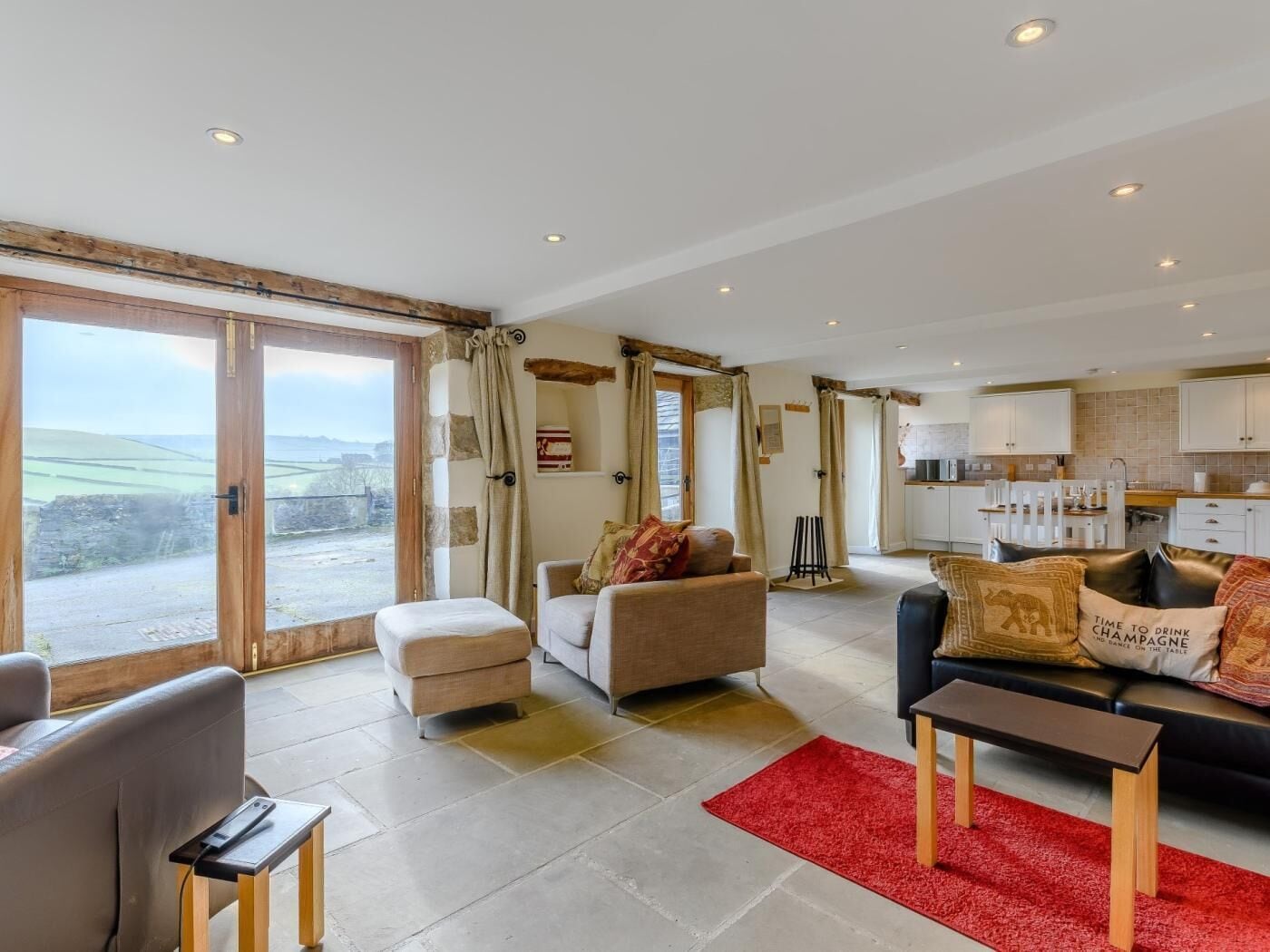 A spacious living area with a large sliding glass door leading to a balcony, a cozy seating area with a sofa and armchairs, and a kitchen in the background.