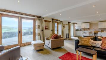 A spacious living area with a large sliding glass door leading to a balcony, a cozy seating area with a sofa and armchairs, and a kitchen in the background.