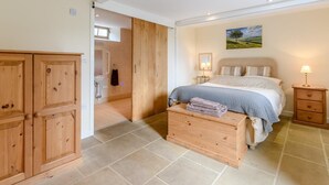Quarto com cama, mesas de cabeceira, guarda-roupa de madeira, banheiro com pia e uma janela.