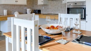 Uma cozinha moderna com armários brancos, bancada de madeira e uma mesa de jantar posta com uma tigela de frutas, copos de vinho e talheres.