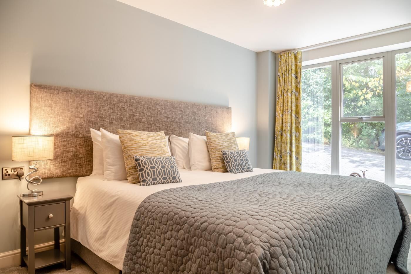 Une chambre à coucher avec un lit, une table de chevet, une lampe et une fenêtre avec des rideaux.