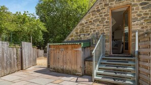 A stone building with a wooden staircase leading to a room with a sofa. - 1 Bed in Matlock (oc-78225) (Paddocks)