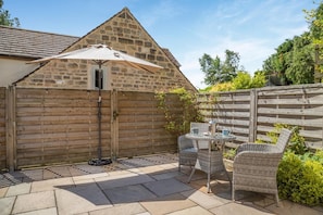 A stone building with a sloped roof, a wooden fence, and a patio area with wicker furniture and a table. - 1 Bed in Matlock (oc-78225) (Paddocks)