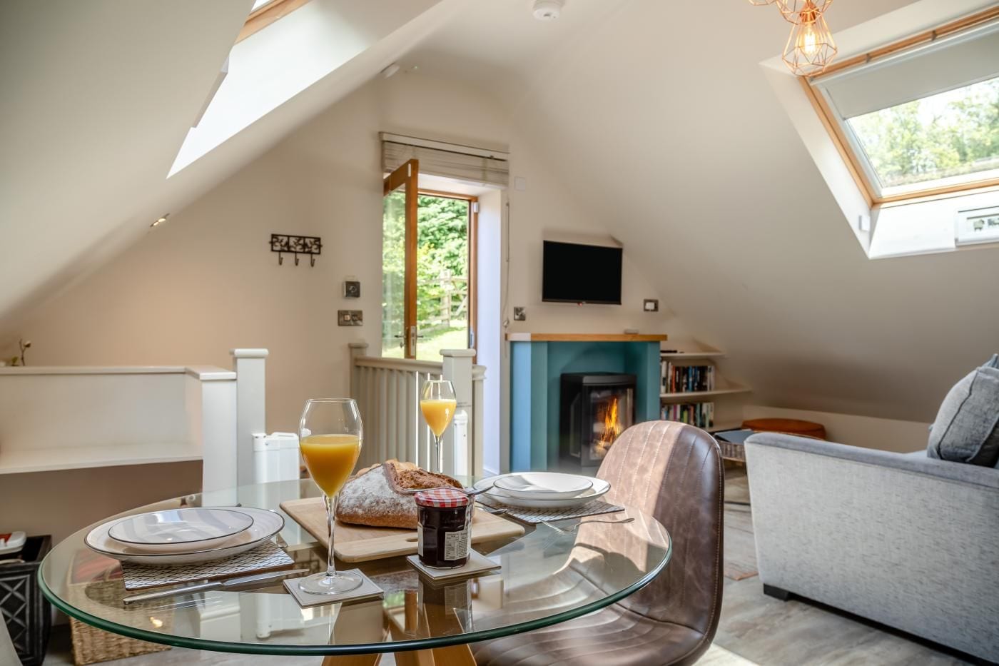 A dining area with a glass table, plates, glasses, and a loaf of bread.