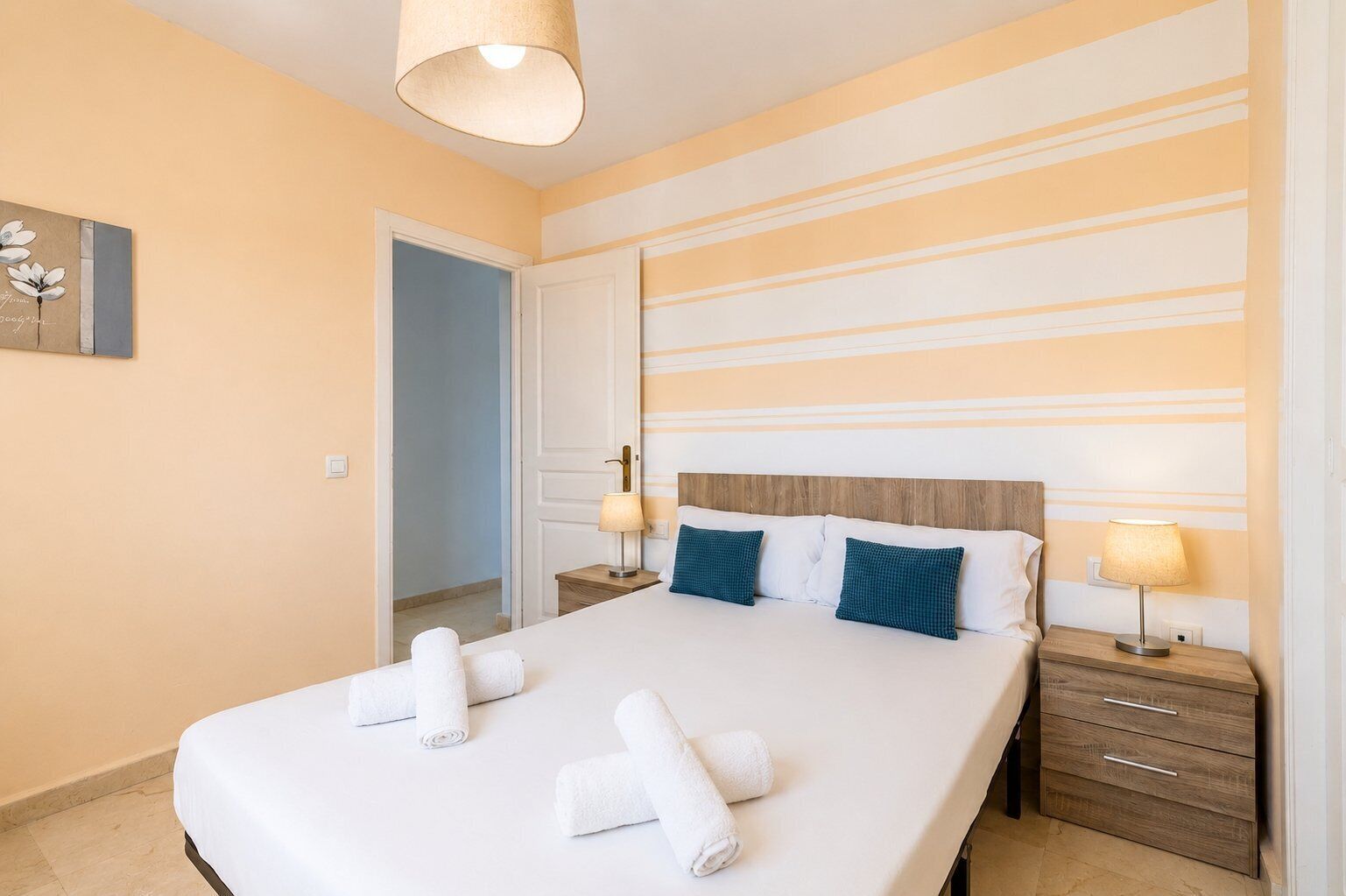 A hotel room with a bed, two bedside tables, a lamp, and a door leading to another room.