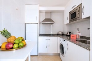 A compact kitchen with a built-in washing machine, a microwave, and a toaster. - GuestReady - Arenas Balcony and Pool (Caleta de Fuste)