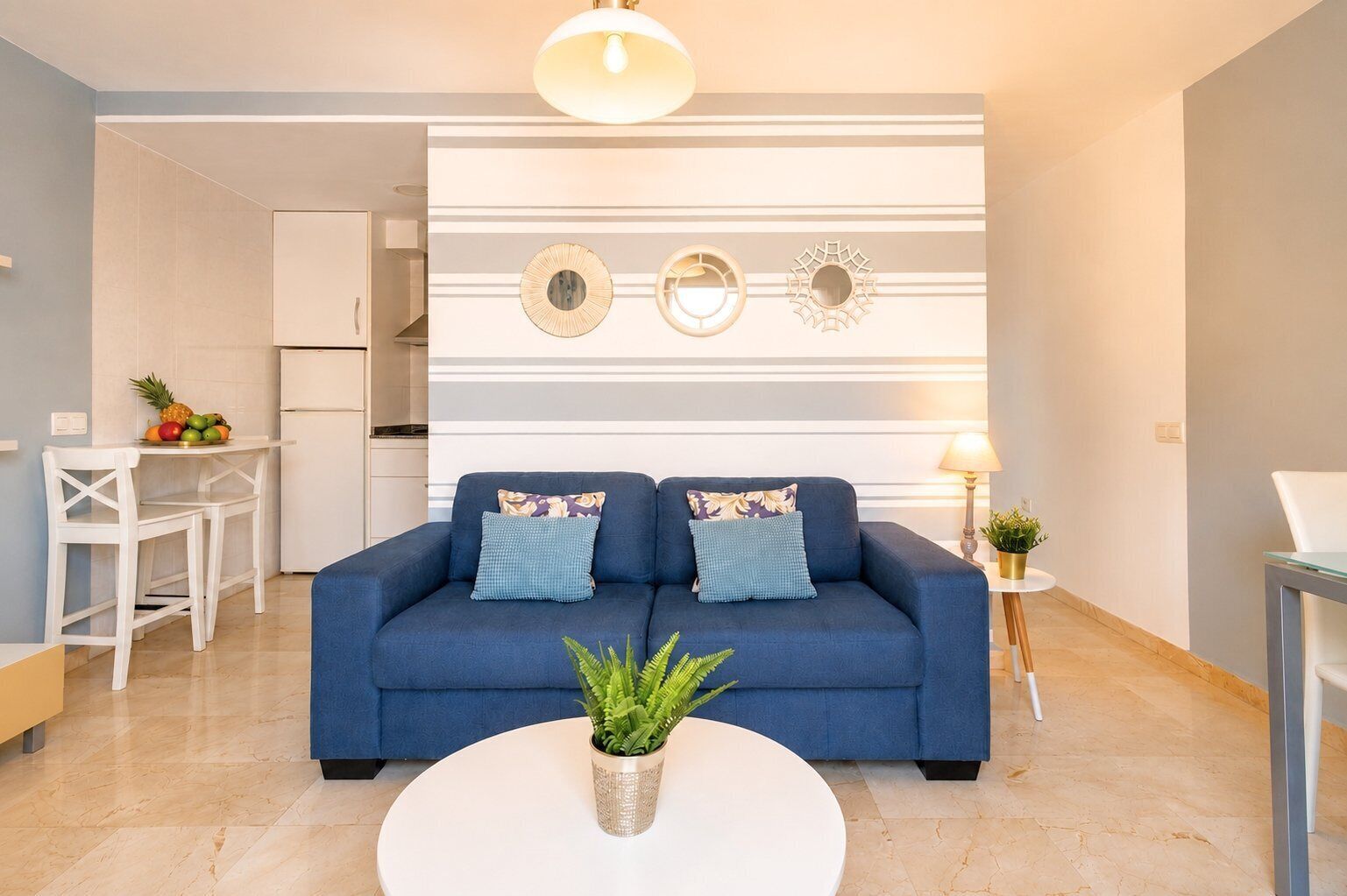 Un saló modern amb un sofà blau, una taula de centre blanca i una cuina al fons.