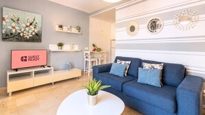 A modern living room with a blue sofa, a flat-screen TV, a coffee table, and decorative wall art. - GuestReady - Arenas Balcony and Pool (Caleta de Fuste)