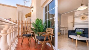 A balcony with wooden chairs and a potted plant, a sliding glass door leading to an interior space with a sofa and a table. - GuestReady - Arenas Balcony and Pool (Caleta de Fuste)