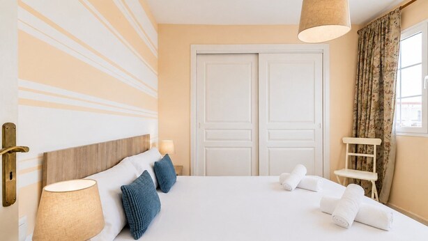 A hotel room with a large bed, two bedside lamps, a wooden headboard, a white door, and a window with curtains. - GuestReady - Arenas Balcony and Pool (Caleta de Fuste)