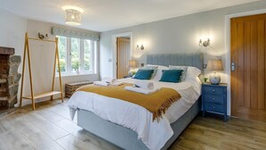 Quarto com cama, mesas de cabeceira, abajur, luminária na parede, janela e lareira.