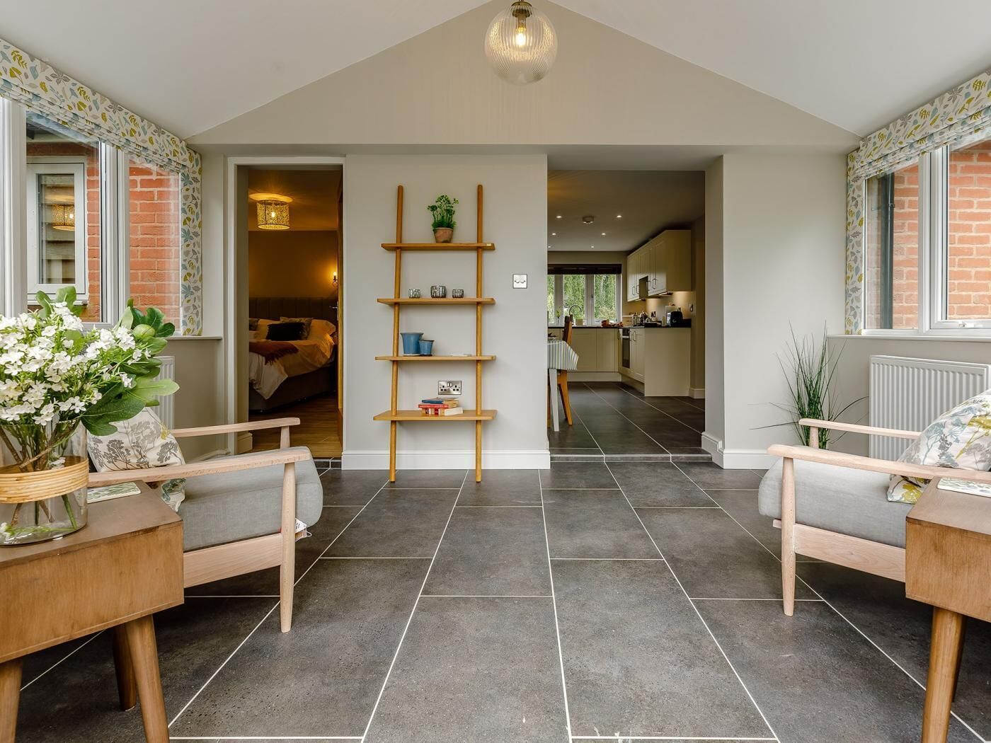 A modern interior with a central wooden shelving unit, a dining area with a bench, and a kitchen visible through an open doorway.