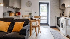 Una cocina moderna con armarios grises, un comedor con mesa y sillas de madera, un sofá con cojines amarillos y una lavadora.