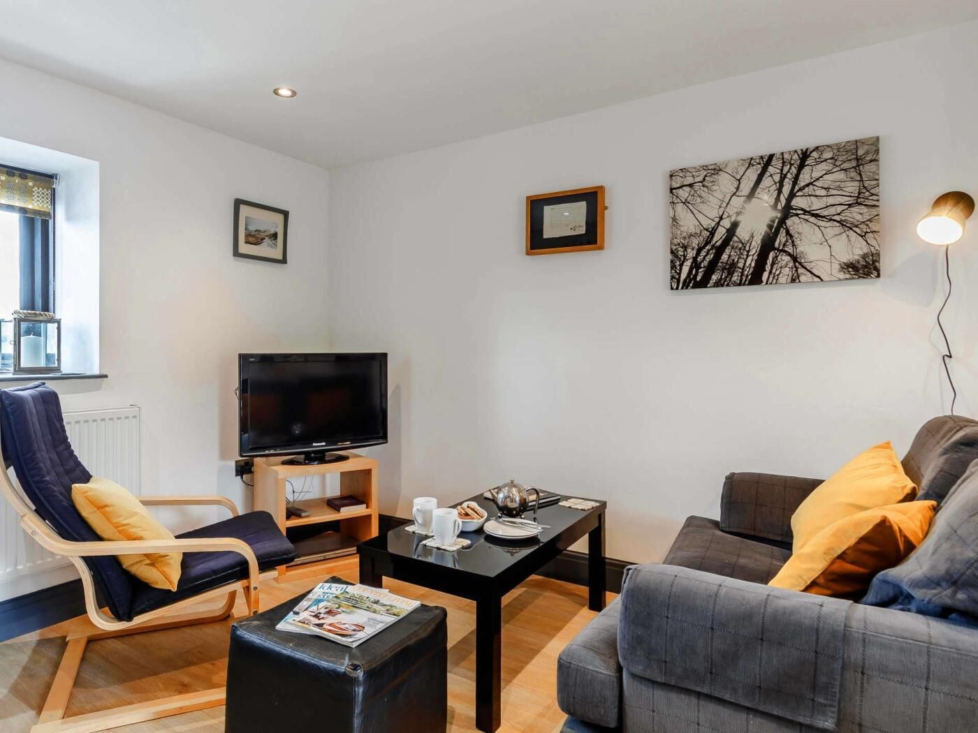 Un salon moderne avec un téléviseur à écran plat, un canapé, un fauteuil, une table basse et un tableau accroché au mur.