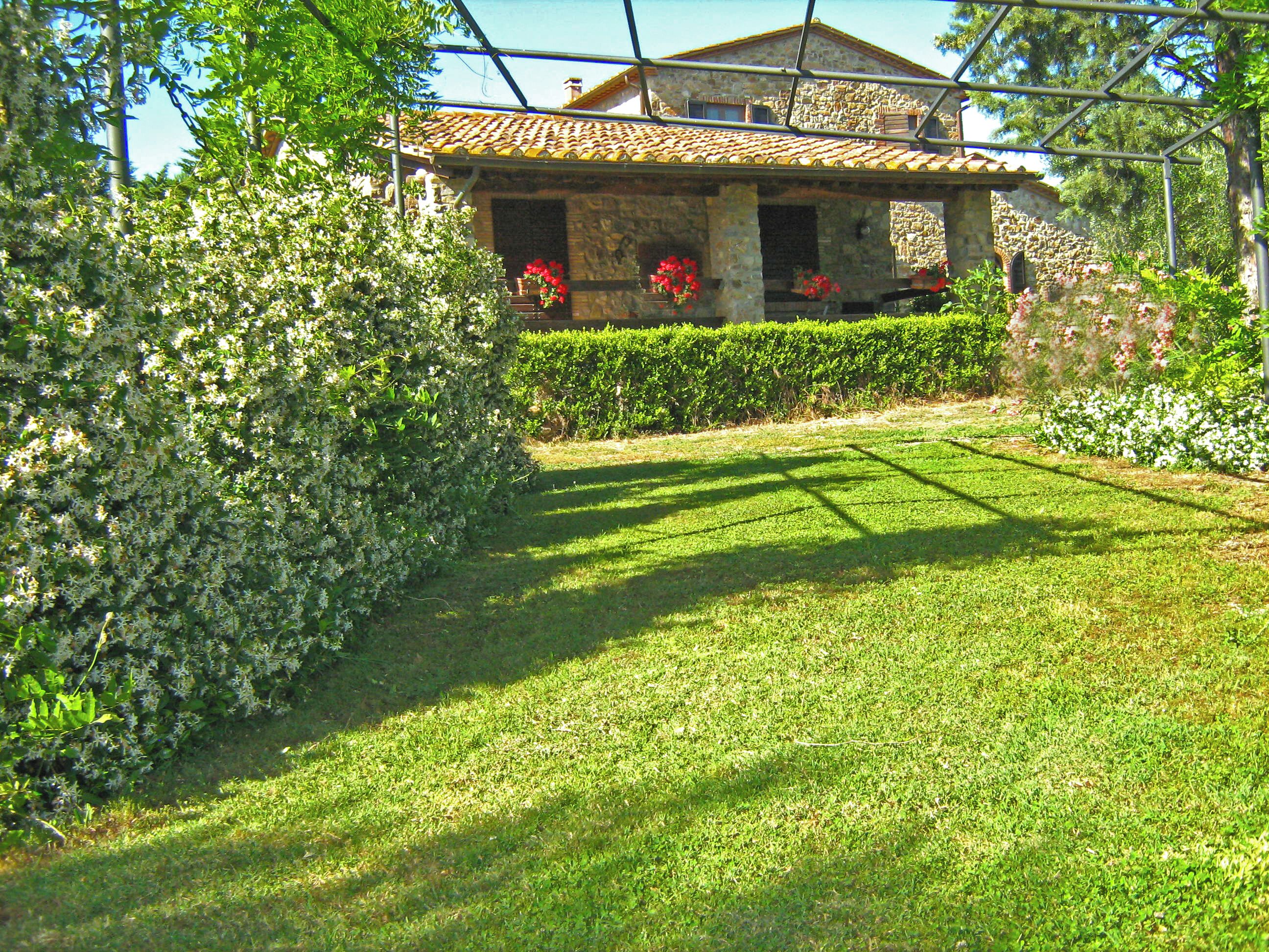 A well-maintained garden with a stone house, a clear pathway, and a variety of plants and flowers.