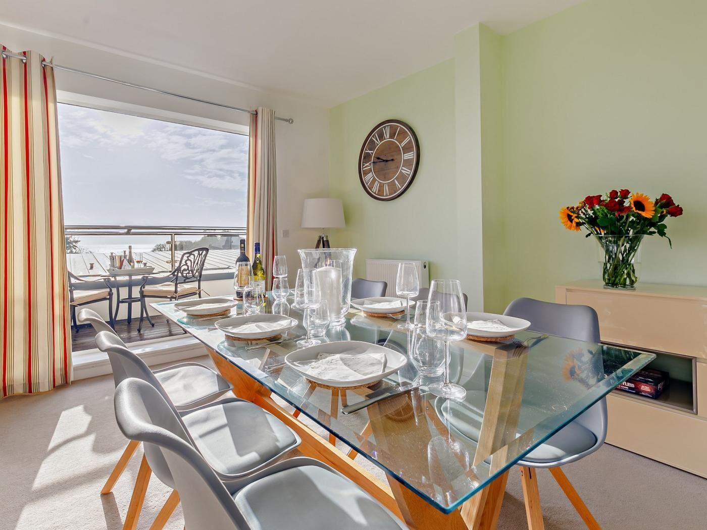A dining area with a glass table, chairs, and a clock on the wall.