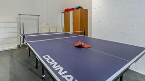 Ein Tischtennistisch mit Netz, Stühle und eine Tür in einem Raum mit weißen Ziegelwänden.