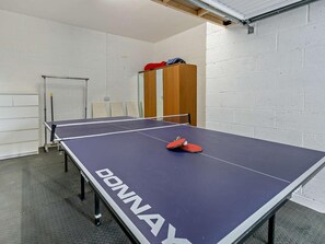 A ping pong table with a net, chairs, and a door in a room with white brick walls. - 3 Bed in St. Austell (oc-65572) (Charlestown)