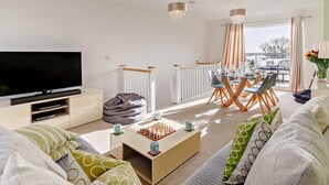 Ein modernes Wohnzimmer mit einem Flachbildfernseher, einem Couchtisch mit Schachspiel, einer Couch und einem Essbereich mit Blick.