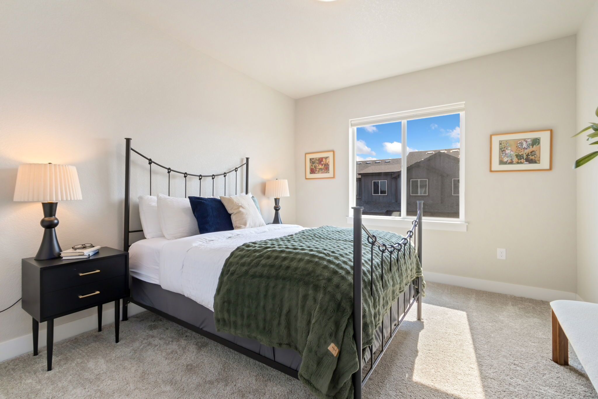 A bedroom with a bed, bedside tables, a window, and a view of a building outside.