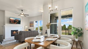 Una sala de estar moderna con chimenea, una mesa de comedor preparada para cuatro personas, un sofá y un televisor montado en la pared.