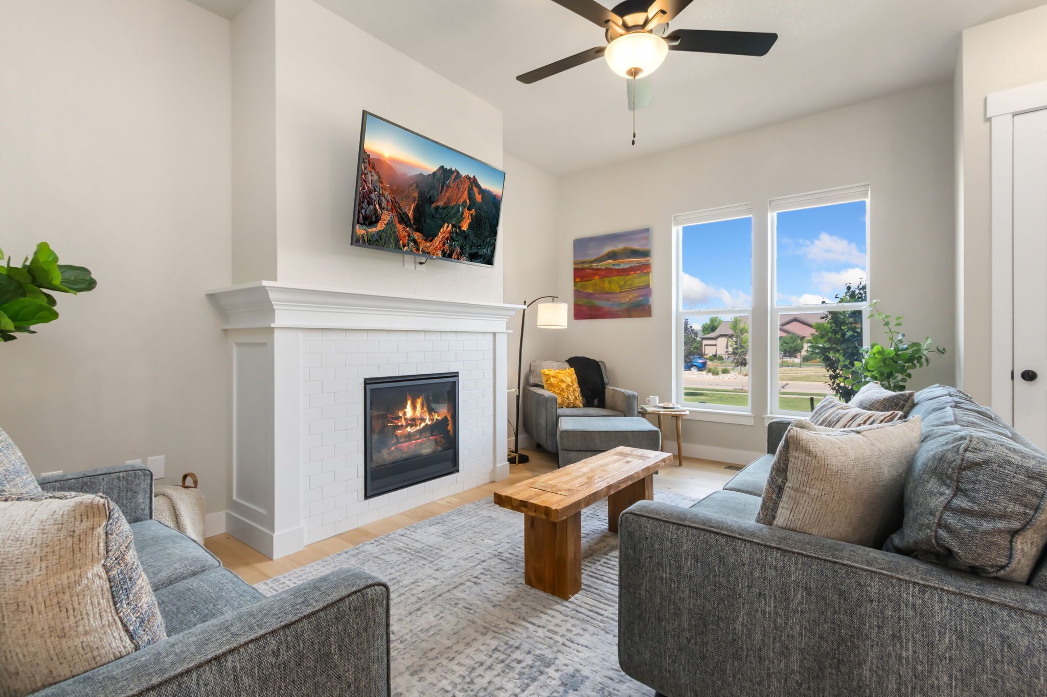 A living room with a fireplace, a ceiling fan, and large windows.