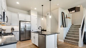 Una cocina moderna con armarios blancos, electrodomésticos de acero inoxidable, una isla central y una escalera que conduce a una zona estilo loft.
