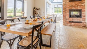 A dining area with a long wooden table, chairs, and a brick fireplace. - 5 Bed in Llanymynech (oc-80686) (Llanymynech)