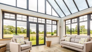 A spacious room with two sofas, a large window, and a view of greenery outside. - 5 Bed in Llanymynech (oc-80686) (Llanymynech)