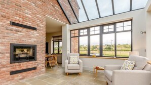 A room with a fireplace, two sofas, a dining table, and large windows offering a view of the countryside. - 5 Bed in Llanymynech (oc-80686) (Llanymynech)
