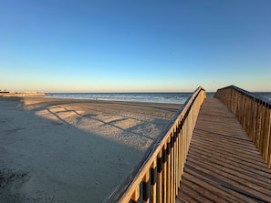 Une promenade en bois qui mène à une plage, avec un ciel dégagé.