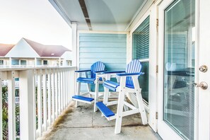Een balkon met twee blauwe Adirondack-stoelen en een witte deur met een metalen handvat.