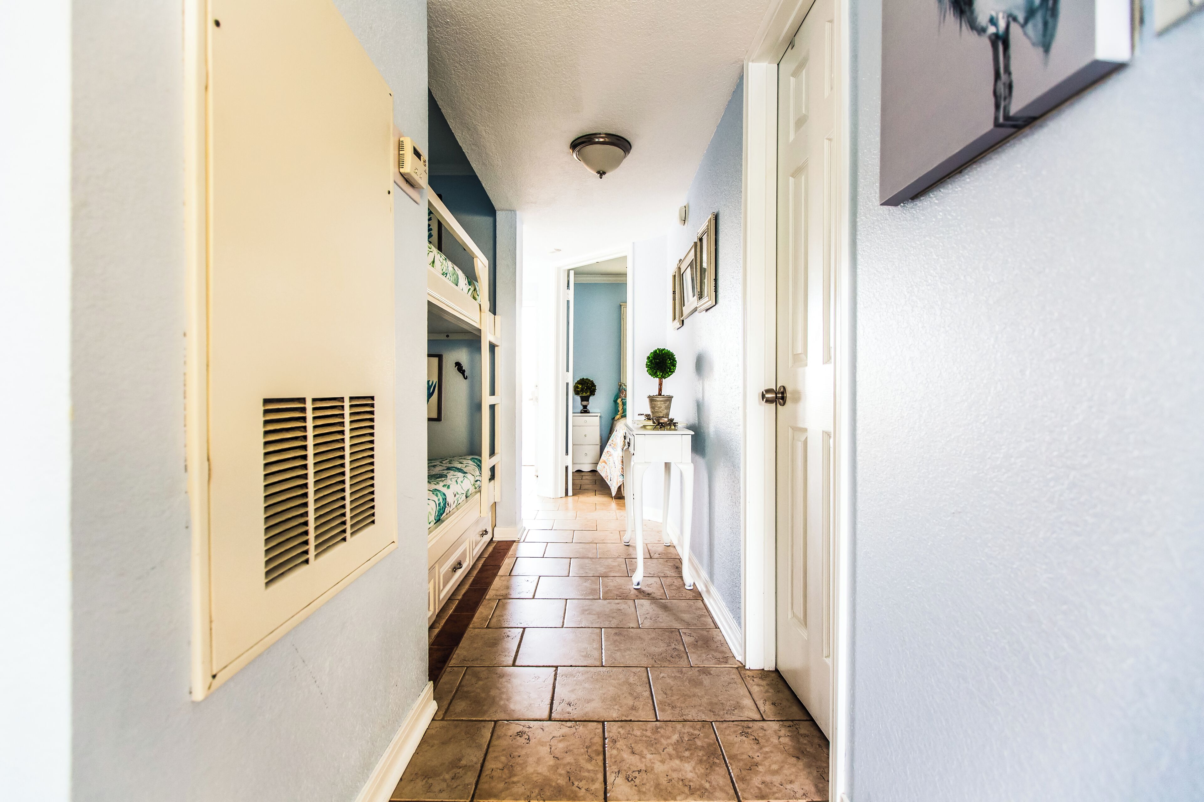 A narrow hallway with a tiled floor, a white door, and a small table with a plant.