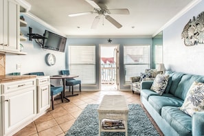 Un salon avec un téléviseur fixé au mur, un ventilateur de plafond, un canapé, une table basse et un coin repas avec une table et des chaises.