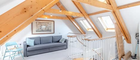 A loft bedroom with a sloped ceiling, a grey sofa, a staircase with a white railing, and skylights.