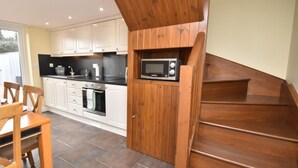 Una cocina con armarios blancos, encimera negra, microondas y una escalera de madera.