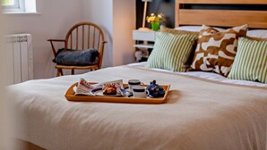 Un letto rifatto con cura, un vassoio con prodotti per la colazione, una sedia e un comodino con una lampada.