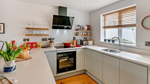 Una cucina moderna con mobili bianchi, forno a incasso, lavello e finestra con persiane.