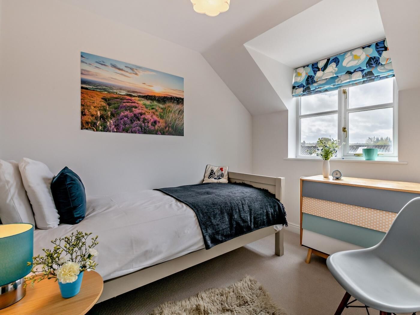 Une chambre à coucher avec un lit, un bureau, une chaise, une fenêtre donnant sur un beau paysage et un tableau accroché au mur.
